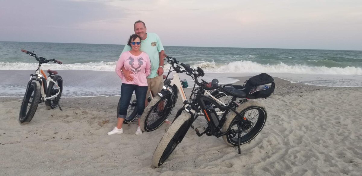Male and Female with electric bikes on the beach.